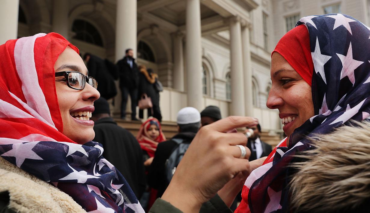 Seorang wanita membantu rekannya memakai kerudung bermotif bendera AS saat perayaan Hari Hijab Sedunia di depan Balai Kota, New York, Rabu (1/2). Hari Hijab Sedunia digagas oleh warga New York bernama Nazma Khan. (Spencer Platt / Getty Images / AFP)