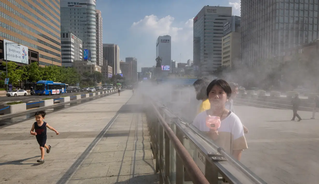 Pejalan kaki mendinginkan diri dengan kipas portabel dan uap air di Gwanghwamun, Seoul, Korea Selatan,  Rabu (1/8). Suhu di Seoul mencapai 39 derajat Celcius atau tertinggi dalam 111 tahun terakhir. (Ed JONES/AFP)