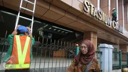 Pengguna jalan melintas di dekat pekerja yang sedang membersihkan dinding Stasiun Cikini di Jakarta, Senin (20/3). (Liputan.com/Immanuel Antonius)