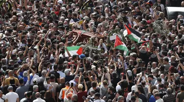 Orang-orang Palestina mengibarkan bendera nasional saat membawa peti mati jurnalis Al-Jazeera Shireen Abu Akleh yang tewas tertembak selama prosesi pemakamannya di dekat Gerbang Jaffa, salah satu gerbang utama Kota Tua Yerusalem, 13 Mei 2022. Shireen Abu Akleh yang merupakan jurnalis senior berusia 51 tahun itu terkena tembakan di kepala ketika meliput serangan Israel di Kota Jenin, di wilayah Tepi Barat yang diduduki pada 11 Mei 2022 lalu. (Ahmad GHARABLI / AFP)