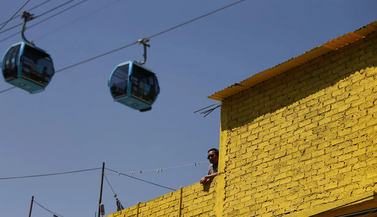 Seorang pria berdiri di atap saat kereta gantung berjalan di antara stasiun Campos Revolucion dan Tlalpexco selama peresmian sistem angkutan umum udara baru yang dijuluki Cablebus di lingkungan Cuautepec, utara Mexico City, Meksiko, Kamis (4/3/2021). (AP Photo/Rebecca Blackwell)