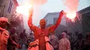 Seorang pria yang tubuhnya berlumuran tepung menyalakan kembang api saat mengikuti perang tepung terigu di kota pelabuhan Galaxidi, Yunani (19/2). (AP/Petros Giannakouris)