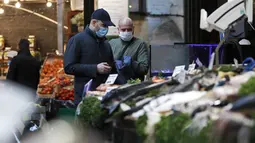 Orang-orang yang memakai masker wajah berbelanja di Borough Market di London selatan selama penguncian nasional (lockdown) ketiga Inggris, Selasa (12/1/2021). Borough Market menjadi tempat pertama yang mewajibkan pemakaian masker di luar ruangan. (AP Photo/Alastair Grant)