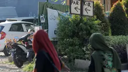Dua wanita muslim berjalan melewati papan izin mendirikan bangunan (biru) di bekas lokasi bom Bali Sari Club di Kuta, Bali, Jumat (26/4). Perdana Menteri Australia Scott Morrison memprotes rencana pembangunan restoran di lahan bekas Sari Club yang merupakan lokasi pemboman Bali (SONNY TUMBELAKA/AFP)