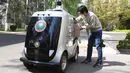 Seorang pria mengambil barang dari mobil pengiriman tanpa awak di Institut Teknologi Beijing, Beijing, China, Senin (6/4/2020). Mobil pengiriman tanpa awak berteknologi 5G ini juga mampu mengenali informasi wajah dan melakukan pengiriman tanpa bersentuhan. (Xinhua/Ren Chao)