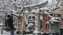 Seorang pria mengambil foto pepohonan yang tertutup salju dan gerbang torii tradisional Jepang di sebuah kuil di Kyoto setelah salju tebal dan angin kencang semalaman mempengaruhi wilayah luas negara itu, Rabu (25/1/2023). Orang-orang diimbau agar bersiap menghadapi salju lebat dan suhu yang rendah serta menahan diri agar tidak keluar rumah untuk urusan yang tidak penting. (Fred Mery / AFP)