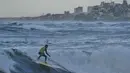 Meski, sepanjang garis pantai menunjukkan kerusakan nyata dengan puing-puing bangunan di sekitarnya. Tampak dalam foto, Khalil Abu Jayyab, warga Palestina, berselancar di pantai Kota Gaza, Minggu, 28 Desember 2025. (AP Photo/Jehad Alshrafi)