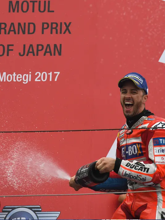 Pembalap Ducati, Andrea Dovizioso menyemprotkan sampanye di atas podium usai memenangi MotoGP Jepang di sirkuit Motegi (15/10). Dovizioso  juara usai terlibat duel sengit dengan Marc Marquez di tikungan terakhir. (AFP Photo/Toshifumi Kitamura)