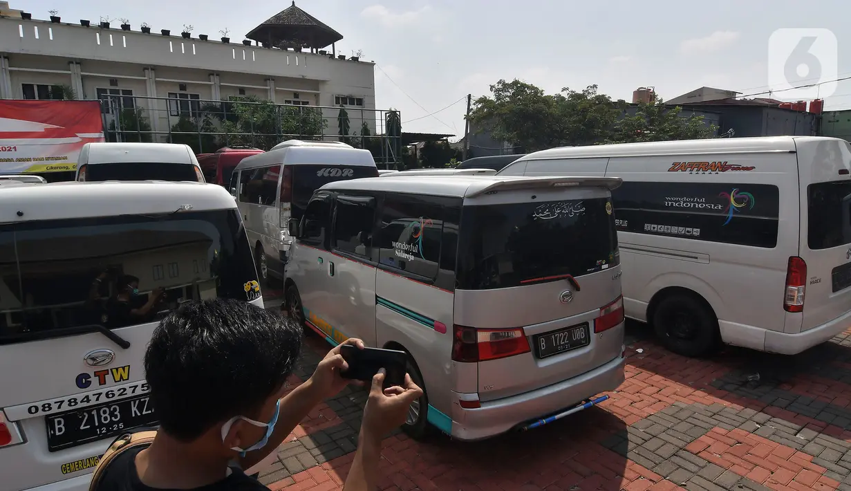 Seorang pewarta mengambil gambar mobil travel gelap yang disita di halaman Polres Metro Kabupaten Bekasi, Jawa Barat, Senin (10/5/2021). Satlantas Polres Metro Bekasi mengamankan 32 travel gelap yang masih beroperasi saat larangan mudik dari tanggal 6-17 Mei 2021. (Liputan6.com/Herman Zakharia)