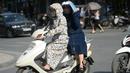 Seorang wanita pengendara motor dan rekannya menggunakan pakaian pelindung saat melintasi pusat kota Hanoi, Rabu (15/6). Vietnam menghadapi gelombang panas dengan suhu hingga mencapai 40 derajat celcius. (Hoang DINH NAM/AFP)