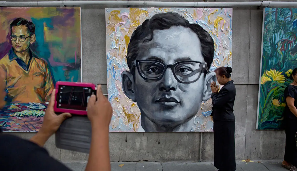 Seorang warga mengambil memotret lukisan mendiang Raja Thailand Bhumibol Adulyadej di luar Grand Palace, Bangkok, Thailand (13/10). Raja Bhumibol Adulyadej meninggal pada 13 Oktober 2016, di usia 88 tahun. (AP Photo/Gemunu Amarasinghe)