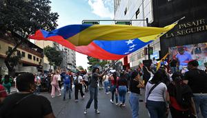 Mereka meneriakkan slogan anti-imperialisme dan menyatakan bahwa Venezuela bukan negara yang akan menyerah. Tampak dalam foto, seorang pendukung mantan Presiden Venezuela, Nicolas Maduro, membawa bendera nasional saat mengikuti aksi unjuk rasa di Caracas pada Minggu 4 Januari 2026. (Juan BARRETO/AFP)