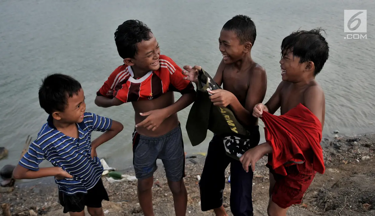 Anak-anak tertawa saat berpakaian usai berenang di Danau Sunter, Jakarta, Selasa (23/7/2019). Anak-anak tetap nekat berenang di Danau Sunter kendati mereka sadar telah dilarang dan dapat membahayakan diri sendiri. (merdeka.com/Iqbal Nugroho)
