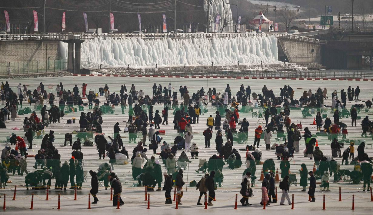Pengunjung dapat memancing ikan trout gunung melalui lubang yang dibuat di atas permukaan sungai yang membeku. Tampak dalam foto, orang-orang memancing melalui lubang-lubang di sungai yang membeku selama festival tahunan memancing di atas es, Hwacheon, Korea Selatan, pada Sabtu 10 Januari 2026. (Shin Yong-ju/AFP)