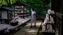 Pengunjung yang mengenakan masker berjalan melewati patung-patung maneki-neko di Kuil Gotokuji, Tokyo, Jepang, Rabu (10/6/2020). Kuil Gotokuji terkenal karena dipercaya sebagai tempat kelahiran maneki-neko, kucing pembawa keberuntungan. (Philip FONG/AFP)