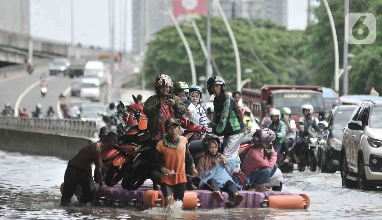 Pengendara sepeda motor menggunakan jasa rakit saat banjir melanda Cempaka Putih, Jakarta, Minggu (23/2/2020). Pengendara memanfaatkan jasa angkutan rakit yang ditawarkan warga agar dapat melewati banjir. (merdeka.com/Iqbal S. Nugroho)