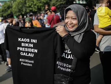 Pedagang memperlihatkan kaus #2019GantiPresiden yang dijajakan saat Car Free Day di kawasan Bundaran HI, Jakarta, Minggu (29/4). Memanasnya suasana politik nasional dimanfaatkan pedagang berjualan atribut #2019GantiPresiden. (Liputan6.com/Faizal Fanani)