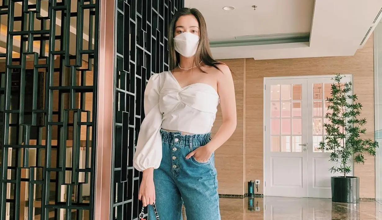 Gunakan one shoulder top berwarna putih, Ranty Maria memilih memadukannya dengan celana jeans. Mantan aktris cilik ini juga terlihat tampil dengan aksesoris berupa kalung sederhana berwarna putih seperti masker yang digunakan. (Liputan6.com/IG/@rantymaria)