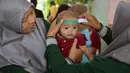 Seorang tenaga kesehatan mengukur lingkar kepala bayi selama program imunisasi massal di Surabaya pada 15 September 2025. (Juni KRISWANTO/AFP)
