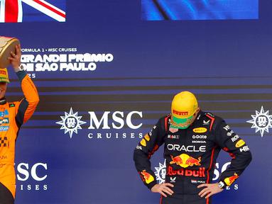 Pembalap Red Bull Racing, Max Verstappen (kanan) tertunduk saat pembalap McLaren, Lando Norrris mengangkat trofi kemenangan dalam Formula 1 GP Sao Paulo di Interlagos, Sao Paulo, Brasil, Minggu (09/11/2025). (AFP/Miguel Schincariol)