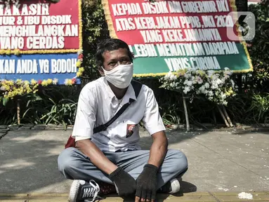 Massa dari Relawan PPDB DKI Jakarta 2020 duduk di depan karangan bunga yang terpajang di Balai Kota DKI Jakarta, Senin (6/7/2020). Karangan bunga itu bentuk kekecewaan terhadap Gubernur Anies Baswedan dan Kadisdik DKI terkait penerimaan siswa baru Jalur Zonasi. (merdeka.com/Iqbal Nugroho)