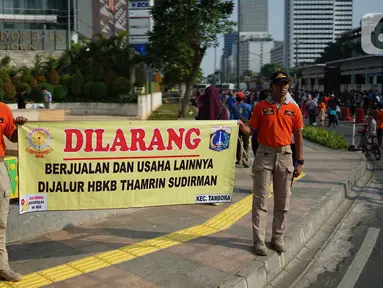 Petugas Satpol PP membentangkan spanduk larangan berjualan di jalur Hari Bebas Kendaraan Bermotor atau Car Free Day, Jakarta, Minggu (3/11/2019). Pemprov DKI melarang PKL berjualan di sepanjang jalur Car Free Day yang selama ini memenuhi badan jalan maupun trotoar. (Liputan6.com/Immanuel Antonius)