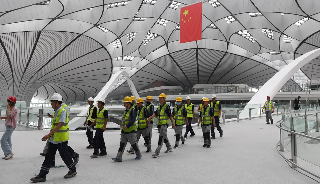 Para pekerja berjalan dalam Terminal Bandara Internasional Daxing Beijing, China, Selasa (9/7/2019). Bandara yang selesai pada 30 Juni 2019 tersebut dijadwalkan dibuka pada 30 September 2019. (GREG BAKER/AFP)