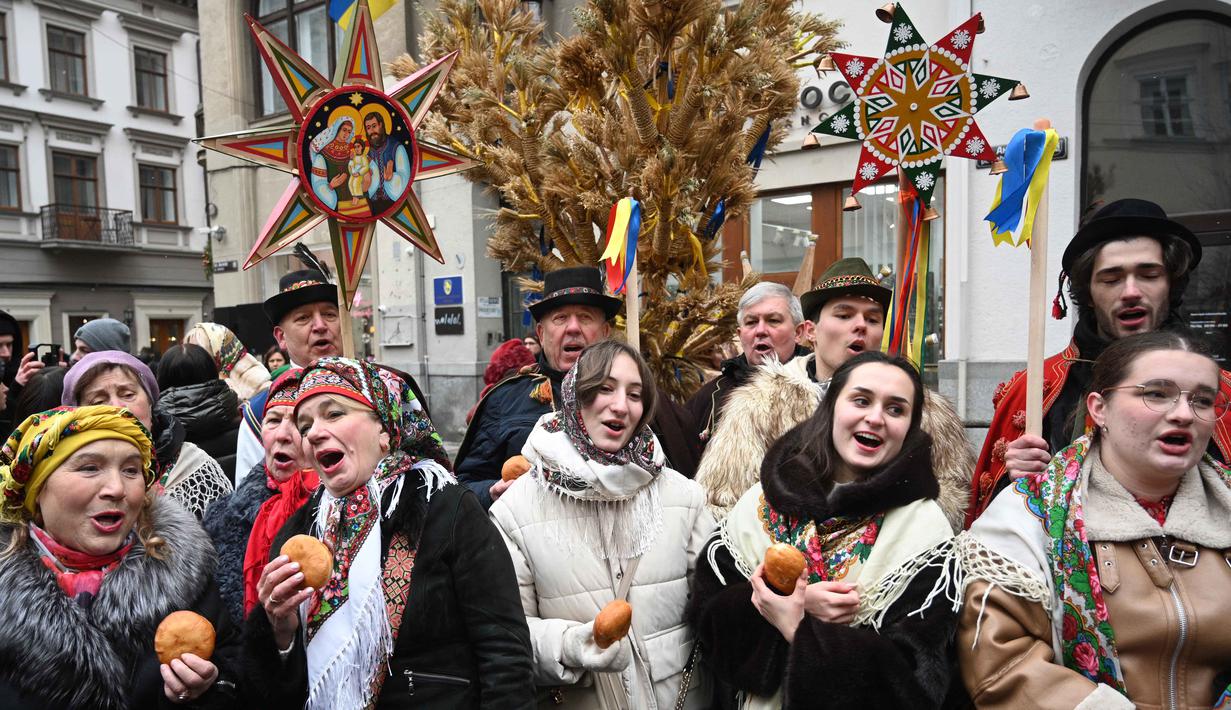 'Didukh' merupakan simbol Natal tradisional Ukraina. Tampak dalam foto, warga Ukraina yang mengenakan pakaian tradisional dan membawa hiasan tradisional Ukraina 'Didukh' menyanyikan lagu-lagu rohani saat mereka mengikuti prosesi Malam Natal di Lviv pada 24 Desember 2025. (YURIY DYACHYSHYN/AFP)