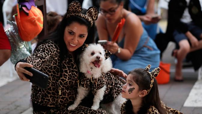 Diana Vargas (kiri) mengambil foto putrinya Naomi dengan anjing mereka Minnie saat mengikuti kontes kostum anjing Halloween tahunan di Coral Gables Museum, Coral Gables, Florida, Amerika Serikat, Kamis (31/10/2019). (AP Photo/Lynne Sladky)