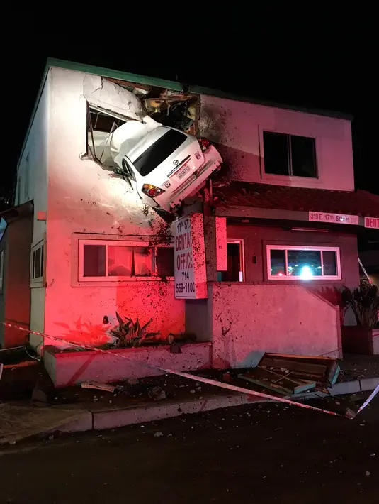 Sebuah mobil tertancap di bangunan lantai dua klinik dokter gigi di Santa Ana, California, Minggu (14/1). Mobil itu melaju kencang hingga terbang ke udara dan menembus bangunan lantai dua hingga melukai dua orang. (Orange County Fire Authority via AP)