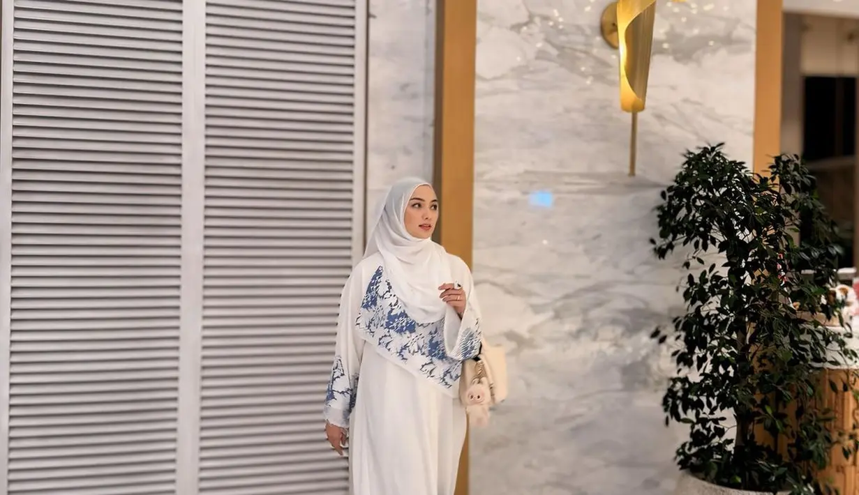 Citra Kirana tampil menawan dibalut gamis putih dengan detail bordir biru di bagian ujung-ujung busananya. Tak berlebihan, ia padukan penampilannya dengan hijab putih polos. [Foto: Instagram/citraciki]