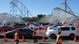 Relawan berjalan saat orang-orang yang telah menerima vaksin berada di dalam kendaraan mereka di pusat vaksinasi COVID-19 drive-thru massal di tempat parkir Six Flags Magic Mountain di Valencia, California, Selasa (2/2/2021). Mario Tama/Getty Images/AFP)