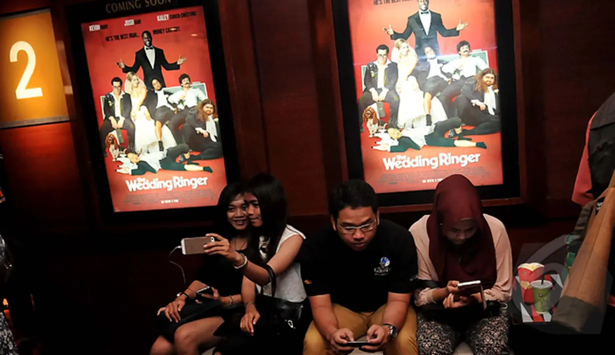 Sambil menunggu studio dibuka, penonton ini selfie sambil duduk dibawah poster film saat Premier Film The Wedding Ringer, Jakarta, Selasa,(17/2/2015) (Liputan6.com/Johan Tallo)