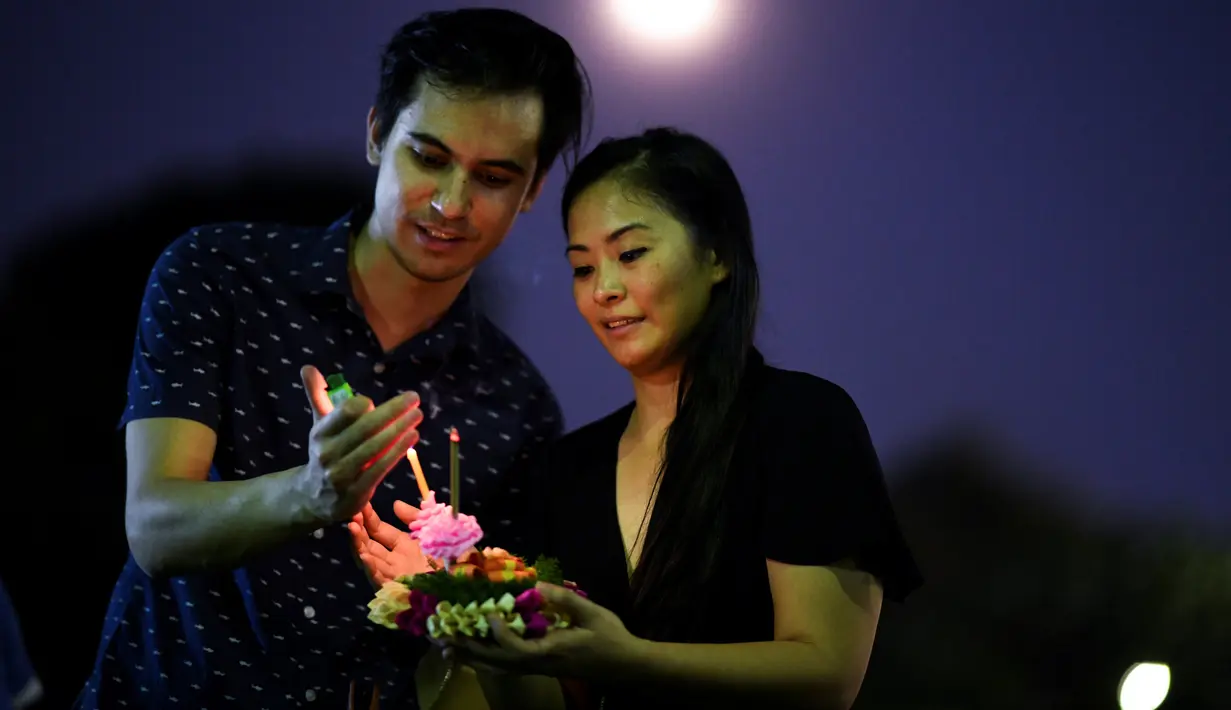 Pasangan bersiap menghayutkan 'krathong' untuk merayakan festival Loy Krathong di sebuah danau di Bangkok, Kamis (22/11). Loy Krathong adalah ritual melarung wadah berbentuk lotus yang didalamnya diberi sesajen, lilin dan dupa. (Jewel SAMAD/AFP)