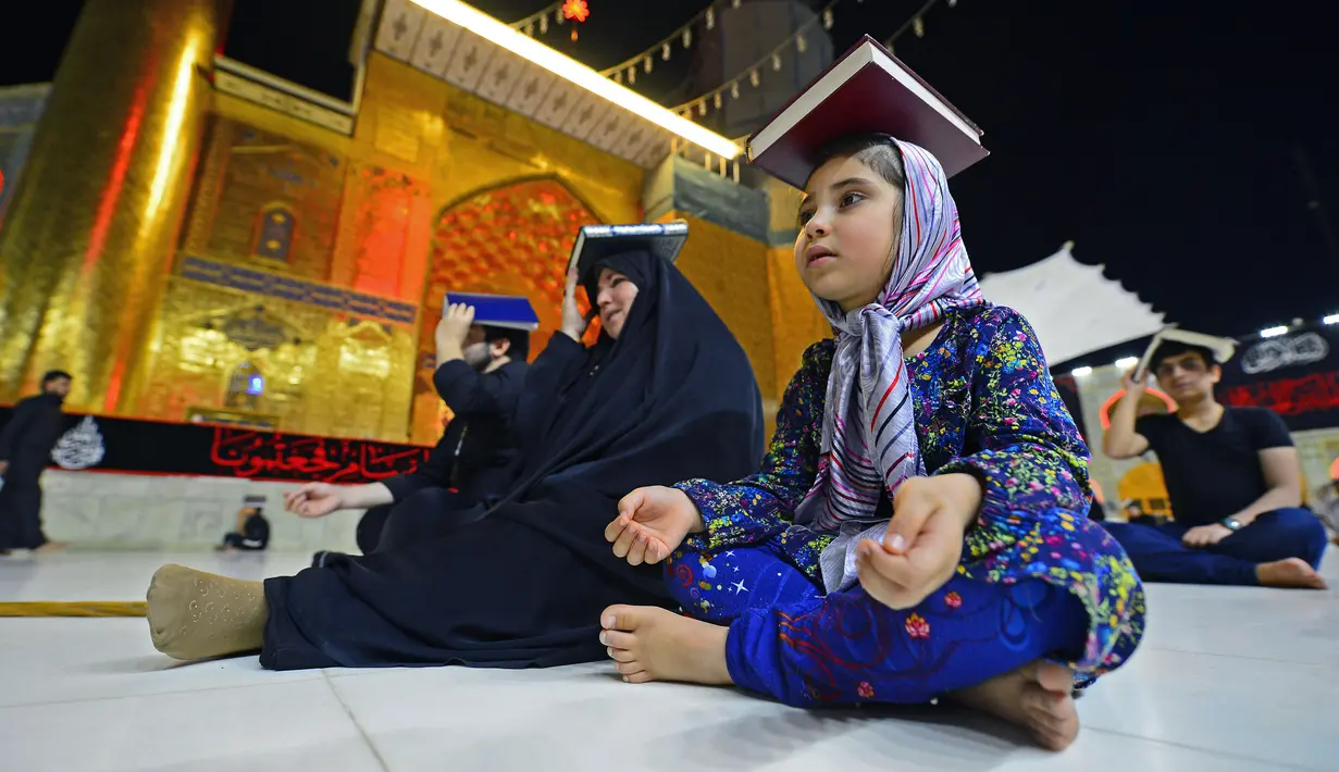 Para jemaah syiah manaruh kitab suci Al-Quran di atas kepala mereka saat menyambut malam lailatul qadar di Makam Suci Imam Ali, Najaf, Irak, Sabtu (16/5/2020). Ritual saat berdoa dan meminta hajat kepada Tuhan ini sudah berlangsung selama berabad-abad lamanya. (HAIDAR HAMDANI/AFP)
