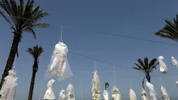 Sejumlah gaun pengantin digantung di antara pohon palem di tepi pantai Beirut, Sabtu (22/4). Sekitar 30 gaun pengantin menggambarkan kondisi mencekam, lusuh dan berwarna pudar sebagai bentuk protes Undang-Undang Pemerkosaan di Lebanon. (PATRICK BAZ/AFP)