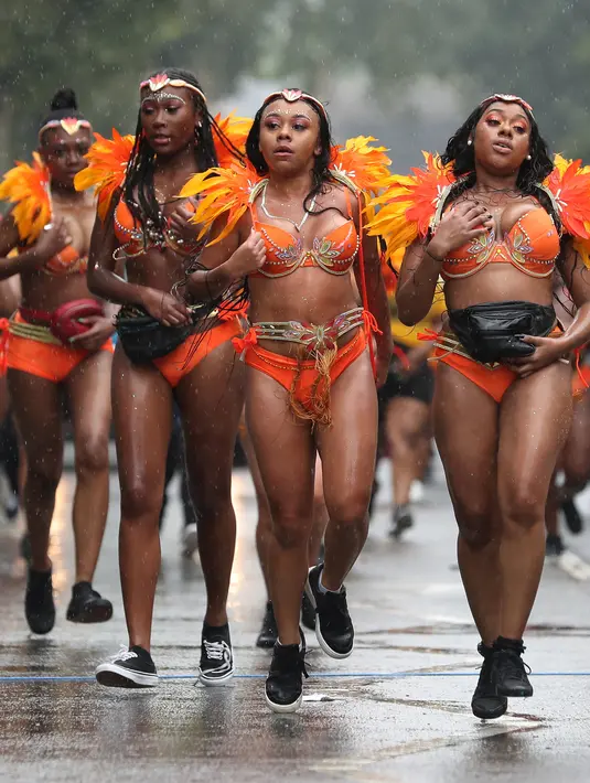 Penari karnaval menari di tengah hujan selama parade hari pertama Karnaval Notting Hill di London barat, Minggu (26/8). Penari mengenakan kostum seksi dan riasan warna-warni saat menggelar karnaval Notting Hill. (AFP/Daniel LEAL-OLIVAS)