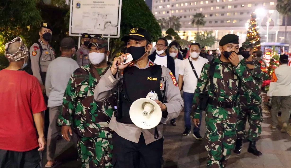 Petugas gabungan melakukan imbauan menggunakan pengeras suara terhadap warga yang berkerumun di kawasan Bundaran HI, Jakarta, Jumat (31/12/2021). Petugas gabungan melarang perayan malam pergantian tahun di wilayah Jakarta untuk mencegah penyebaran COVID-19. (Liputan6.com/Angga Yuniar)