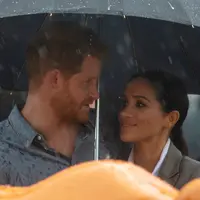 Pangeran Harry dan Meghan Markle berlindung di bawah payung saat piknik di Victoria Park, Dubbo, Australia, Rabu (17/10). Ini adalah hari kedua Pangeran Harry dan Meghan Markle dalam kunjungannya ke Australia. (Ian Vogler/Pool via AP)