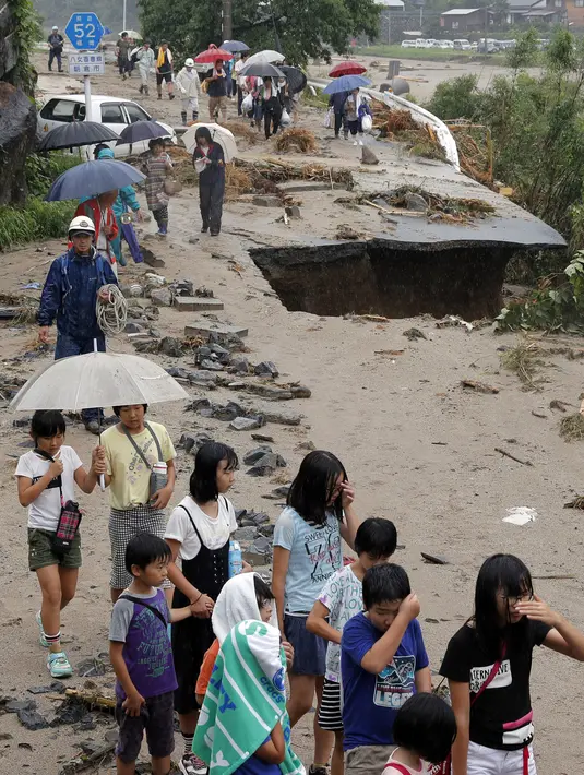 Warga melintasi jalanan yang rusak untuk mengungsi saat banjir merendam daerah Asakura di prefektur Fukuoka, Kamis (6/7). Sedikitnya 15 orang hilang akibat badai ekstrem yang melanda selatan Jepang sejak kemarin. (Takuto Kaneko/Kyodo News via AP)