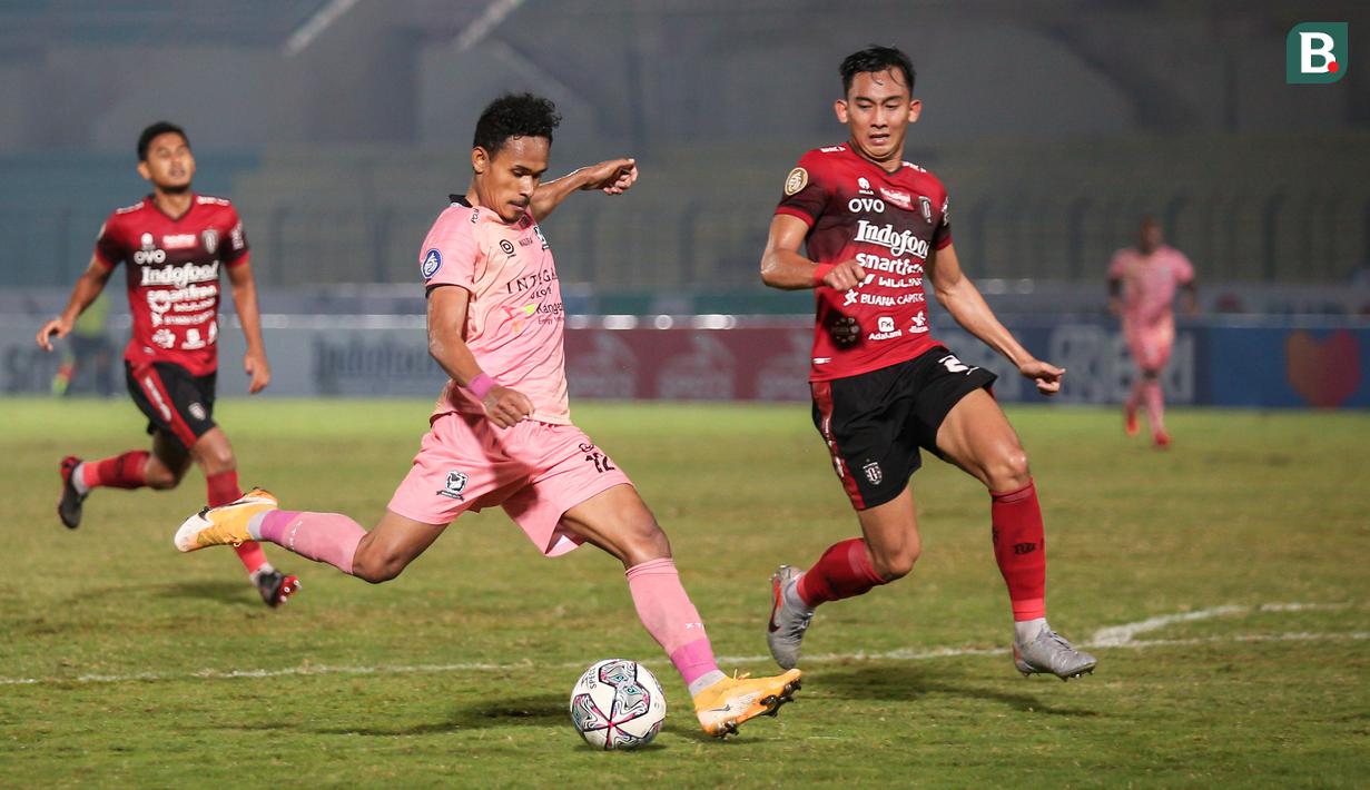 Pemain Madura United, Haris Tuharea (tengah) melepaskan tendangan dibayangi pemain Bali United, Komang Tri Arta dalam laga pekan ke-16 BRI Liga 1 2021/2022 di Stadion Sultan Agung, Bantul, Kamis (09/12/2021). (Bola.com/Bagaskara Lazuardi)
