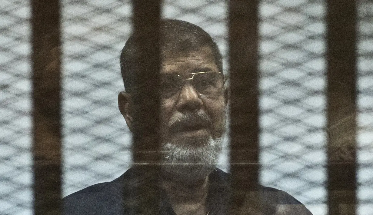 Mantan Presiden Mesir Mohammed Morsi berdiri di belakang jeruji besi saat menjalani sidang di Kairo, Mesir, 16 Juni 2015. Pria berusia 67 tahun tersebut meninggal saat menghadiri sesi pengadilan atas tuduhan spionase. (Khaled DESOUKI/AFP)