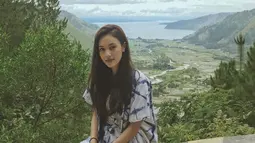 Pemeran Mia di film Yowis Ben 2 ini terlihat sangat cantik berpose dengan latar belakang Danau Toba. Menggunakan pakaian putih bercorak biru, rambutnya yang panjang tampak memesona. (Liputan6.com/IG/@anggikabolsterli)