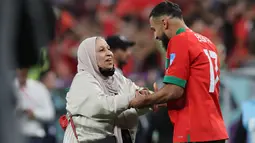 Gelandang Maroko #17 Sofiane Boufal (Kanan) diberi selamat oleh ibunya setelah lolos ke semifinal dengan mengalahkan Portugal pada babak 8 besar Piala Dunia 2022 di Stadion Al-Thumama di Doha, Sabtu (10/12/2022). Boufal dan ibunya juga saling melepaskan senyuman saat mereka saling menatap. (KARIM JAAFAR / AFP)