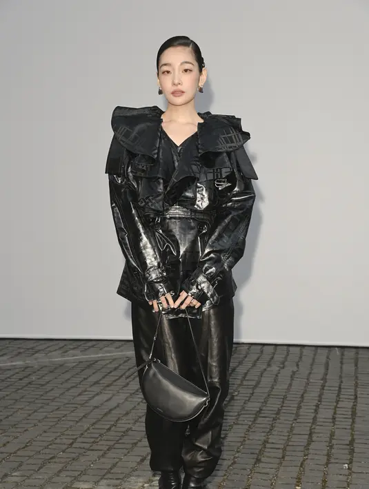 Kim Min-ha menghadirkan interpretasi paling avant-garde dengan jaket bergaya trench berbahan metalik hitam bermotif kotak-kotak. Lengkap detail kerah berlapis oversized yang dramatis, dipadukan celana kulit hitam dan tas selempang hitam. [dok. Burberry]