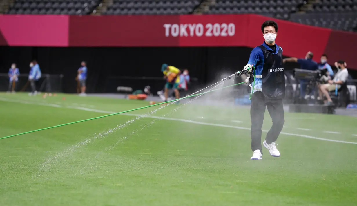 Petugas menyemprotkan disinfektan ke lapangan untuk menghentikan penyebaran virus corona COVID-19 jelang pertandingan sepak bola putaran pertama grup C putra Olimpiade Tokyo 2020 antara Argentina dan Australia di Sapporo Dome, Sapporo, Jepang, Kamis (22/7/2021). (ASANO IKKO/AFP)