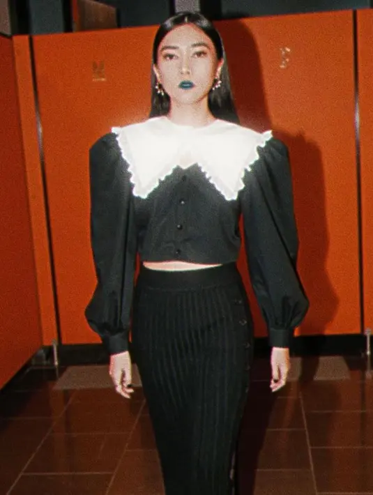 Isyana memadukan atasan warna hitam dengan detail kerah bib ruffle yang dipadukan dengan rok rajut dengan potongan slit warna senada. (Instagram/isyanasarasvati).