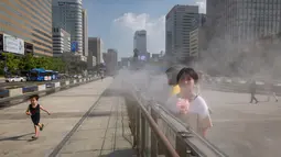 Pejalan kaki mendinginkan diri dengan kipas portabel dan uap air di Gwanghwamun, Seoul, Korea Selatan,  Rabu (1/8). Suhu di Seoul mencapai 39 derajat Celcius atau tertinggi dalam 111 tahun terakhir. (Ed JONES/AFP)