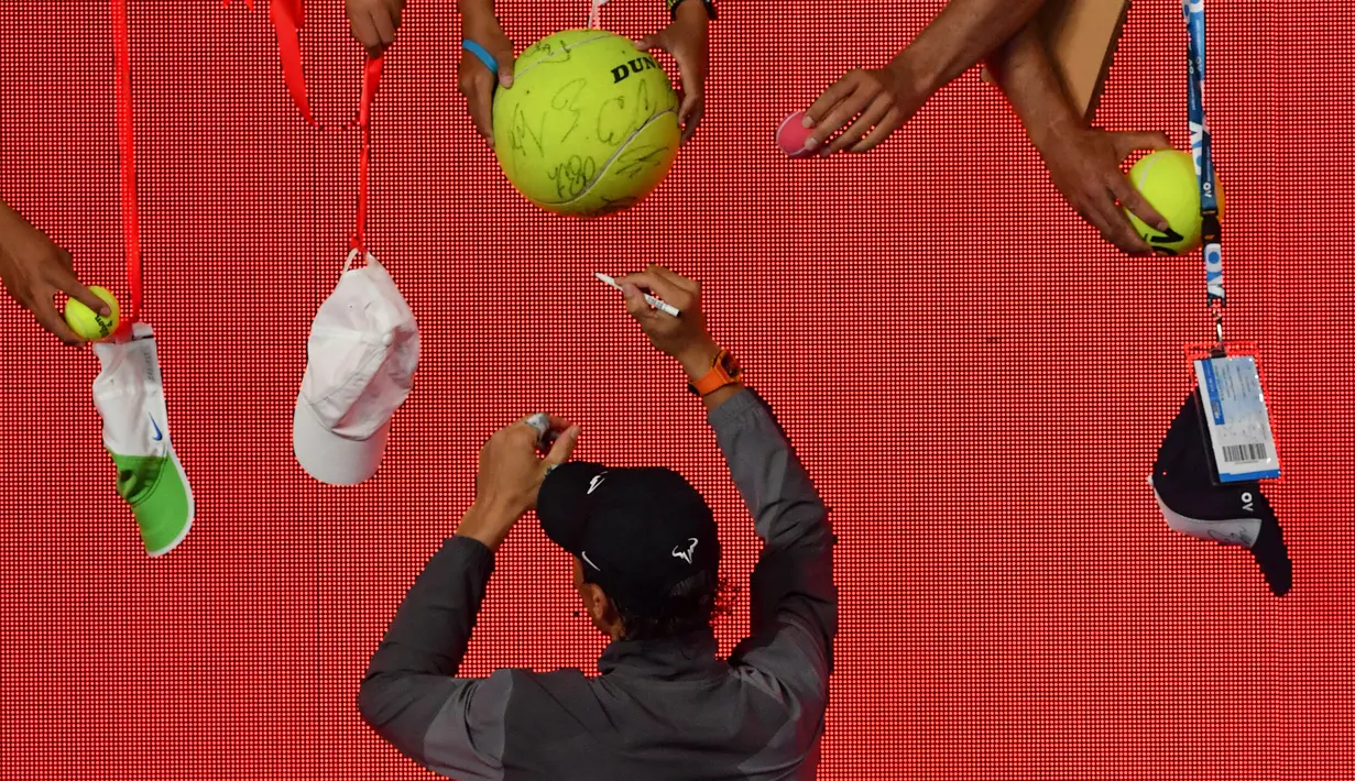 Petenis asal Spanyol, Rafael Nadal memberikan tanda tangan kepada penggemarnya setelah menang atas Matthew Ebden dari Australia pada pertandingan tunggal putra turnamen Australia Terbuka di Melbourne, Rabu (16/1). (Photo by Peter PARKS / AFP)