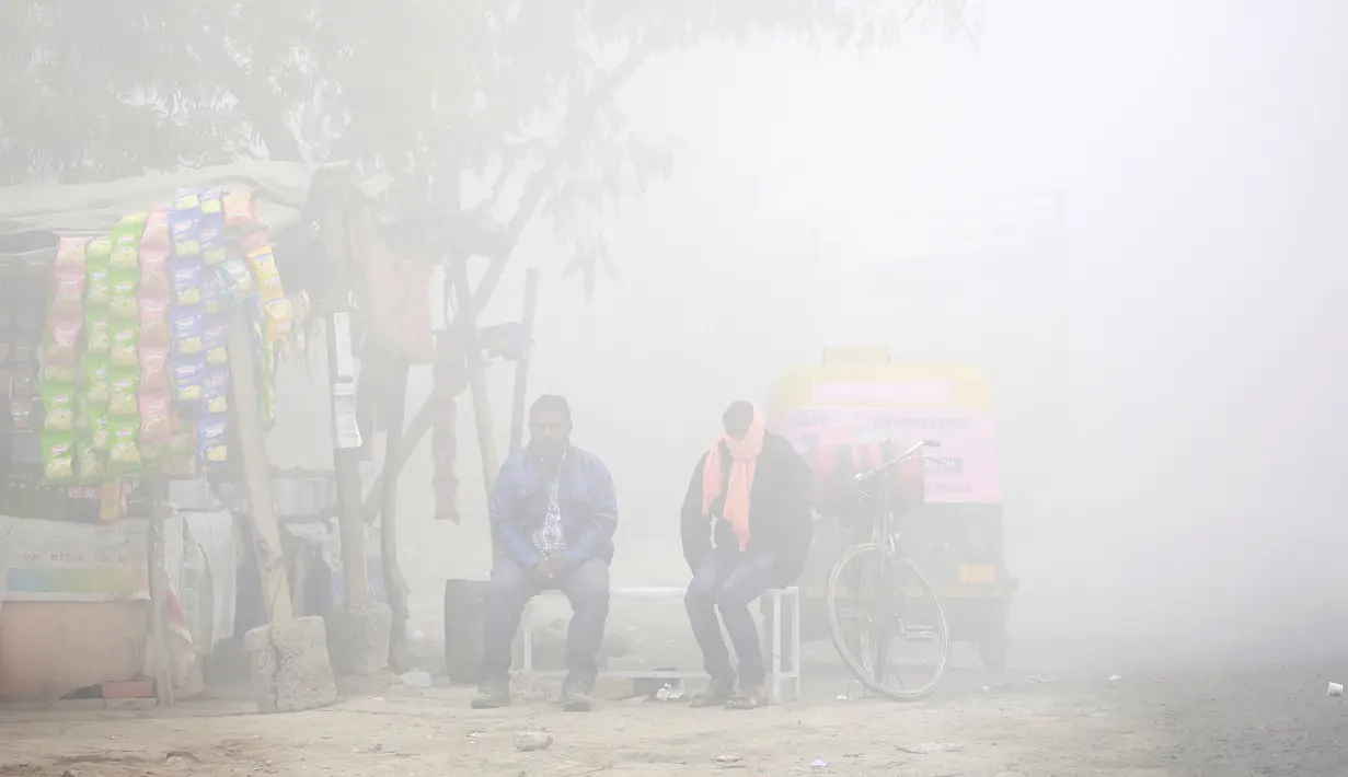 Warga duduk di samping toko saat kabut tebal akibat polusi menyelimuti  Delhi, India (1/12). Kabut ini diklaim sebagai kabut asap terparah yang dialami oleh New Delhi dalam 17 tahun yang telah mengurangi jarak pandang. (REUTERS/Cathal McNaughton)